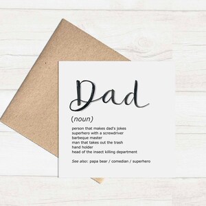 May include: A white greeting card with the word "Dad" in a black script font, with a definition below. The card is inside a brown envelope. The definition includes phrases like "makes dad's jokes" and "superhero with a screwdriver."