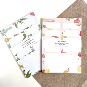 May include: Two meal planners with watercolor illustrations. One features eucalyptus and floral designs, the other has strawberries and oranges. Both have sections for daily meal planning and the text "MEAL PLANNER" and "Designed and Printed in Australia".