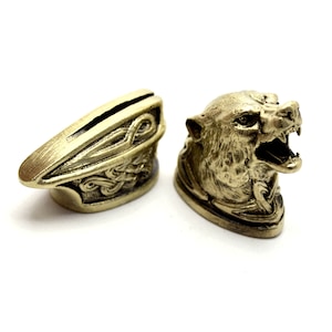 May include: Two decorative metal knife handles. One handle is a wolf's head with an open mouth and the other is a simple, ornate design.