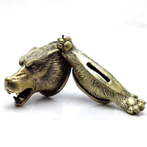 Op de afbeelding: Een gouden metalen zwaardhandvat met een gedetailleerd ontwerp van een wolfskop. Het handvat bestaat uit twee delen, met de kop van de wolf aan de ene kant en het lichaam van de wolf aan de andere kant.