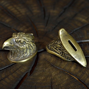 Puede incluir: Dos accesorios de espada de latón, uno con forma de cabeza de águila y el otro con un diseño ornamentado.