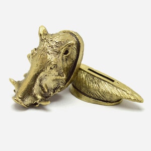 May include: A gold-colored metal knife handle with a detailed sculpture of a warthog head. The handle is attached to a gold-colored metal blade with a decorative design.
