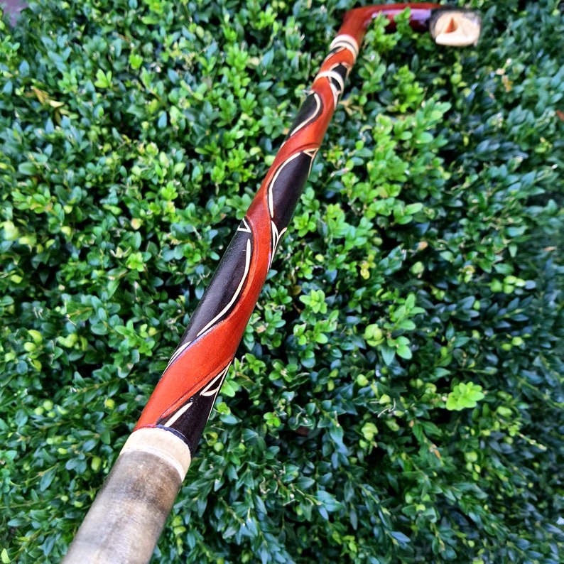 May include: A wooden walking stick with a red, black and white design. The stick is carved with intricate patterns and has a smooth, polished finish.