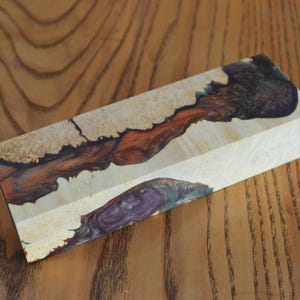 May include: A block of wood with a unique, colorful pattern. The wood is light brown with streaks of purple, red, and black.