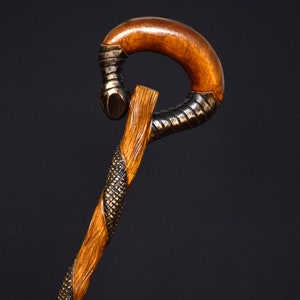 Puede incluir: Un bast&oacute;n de madera con un mango curvo &uacute;nico. El mango est&aacute; hecho de madera oscura y tiene un dise&ntilde;o texturizado en forma de serpiente. El bast&oacute;n est&aacute; hecho de madera clara y tiene una veta natural.