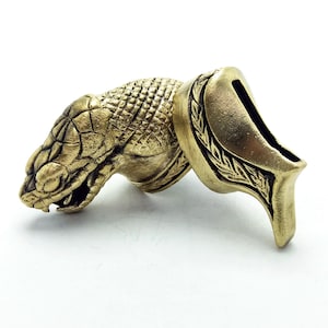 May include: A brass snake head and a brass decorative piece with a leaf design. The snake head is detailed with scales and has a menacing expression. The decorative piece has a smooth surface and a leaf pattern.