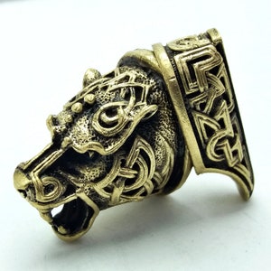 May include: A gold-coloured metal wolf head pendant with intricate Celtic knotwork designs. The pendant is detailed with a textured surface and a raised wolf head.