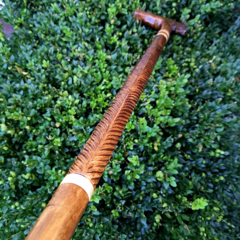 May include: A wooden walking stick with a carved design and a white band near the handle.