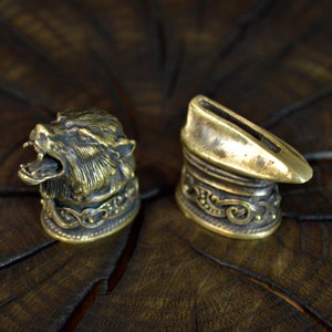 May include: Two ornate metal knife handles. One handle features a detailed wolf head design, while the other is a simple, curved shape with intricate engravings.