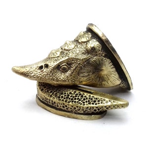 May include: A gold-coloured metal ornament shaped like a stylised fish with a textured surface. The ornament is in two pieces, with the top piece fitting over the bottom piece.