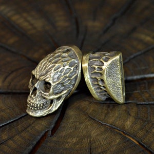 May include: Two brass skull-shaped bottle stoppers with a textured surface.