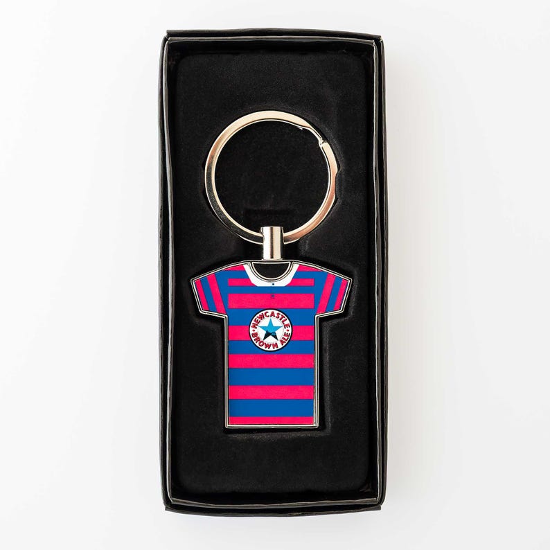 May include: Keyring featuring a miniature soccer jersey with blue and red stripes. The jersey has a circular emblem with text and a star. The keyring is silver and comes in a black box.