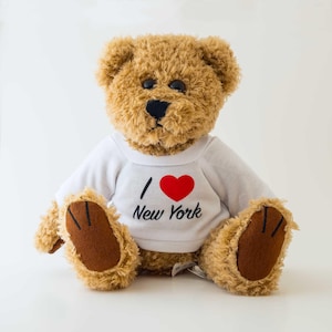May include: A plush teddy bear with brown fur and a white shirt. The shirt features a red heart and the text "I Love New York" in black. The bear has a black nose and brown paws.