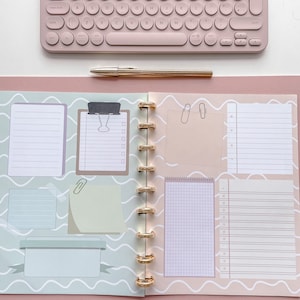 May include: An open planner with a light green and white wave pattern on the left page and a light pink and white wave pattern on the right page. The planner has gold rings and includes various blank and lined sections for writing and note-taking.