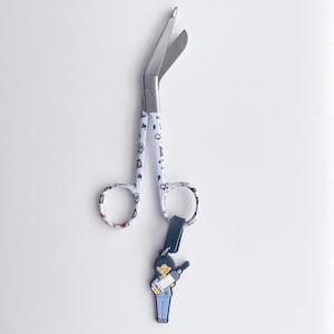 May include: White medical scissors with a colourful pattern of medical symbols and a black and white cartoon nurse keyring.