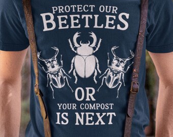 May include: Dark blue t-shirt with the slogan "PROTECT OUR BEETLES OR YOUR COMPOST IS NEXT" in white. The design includes beetle illustrations. Brown leather suspenders are worn over the shirt.