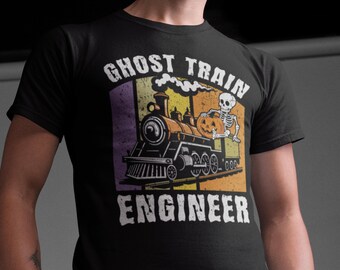May include: A black short-sleeved t-shirt featuring a graphic print of a steam locomotive with a skeleton holding a pumpkin. The text GHOST TRAIN ENGINEER is printed in white above and below the train, set against a background of vertical stripes.