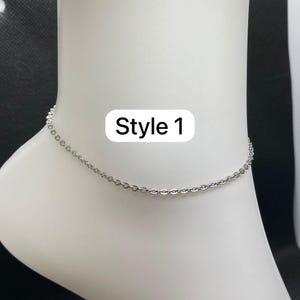 May include: A silver chain anklet, labelled 'Style 1', is shown on a white foot mannequin. The fine chain is made of small, linked segments. The background is black.