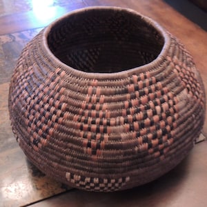 May include: A large, round, woven basket with a brown and pink pattern. The basket is made of natural materials and has a wide opening.