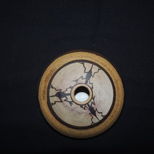 May include: A round ceramic dish with a brown rim and a white centre. The centre has a design of three stylised birds in black, with a small hole in the centre.