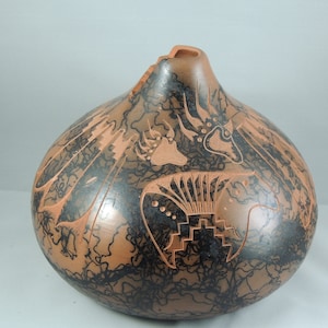 Puede incluir: Una olla de barro marrón con diseños pintados en negro. Los diseños incluyen una huella de pata de oso, un pájaro y un patrón geométrico.