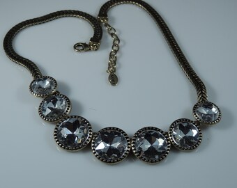 May include: A gold chain necklace with a row of six clear crystal stones set in gold bezels. The necklace has a lobster clasp closure and a small tag with the word "LOFT" on it.