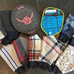 May include: A collection of paddleball accessories, including a black paddle with a pink logo and several fleece wristbands in various patterns and colors. One wristband has white stripes, and another has a leopard print.