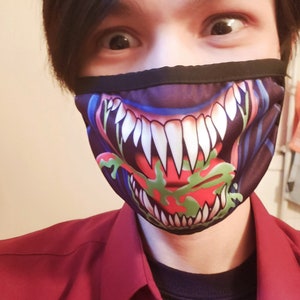 May include: A person wearing a black face mask with a graphic print of a monster's mouth with sharp teeth and a green tongue.