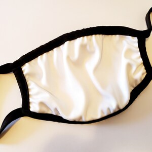 May include: A white face mask with a black elastic band and black trim around the edges.