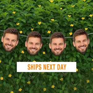 May include: A decorative garland featuring six identical cutouts of a smiling man with a beard, suspended on a thin white string. The cutouts are arranged horizontally against a background of green leaves with small yellow flowers.