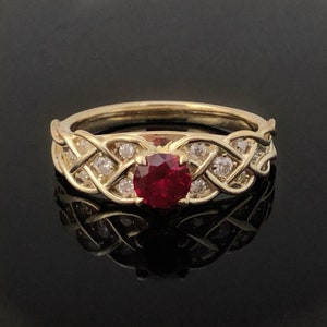 May include: A gold ring with a red ruby gemstone surrounded by smaller diamonds. The ring features a braided design.