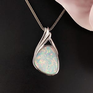 Puede incluir: Un collar de cadena de plata con un colgante que presenta una piedra preciosa de ópalo blanco engastada en un diseño de remolino de plata.