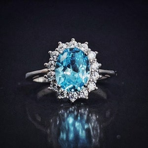 Peut inclure: Une bague en argent avec une grande topaze bleue ovale entourée d'un halo de petits diamants.