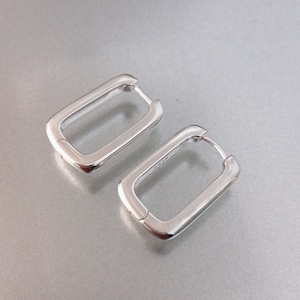 May include: A pair of silver rectangular hoop earrings. The earrings are made of a thick, smooth metal and have a simple, modern design.
