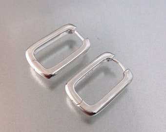 May include: A pair of silver rectangular hoop earrings. The earrings are made of a thick, smooth metal and have a simple, modern design.