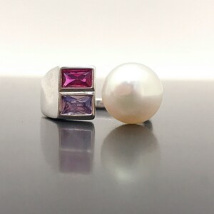 May include: A silver ring with two rectangular gemstones, one pink and one purple, and a white pearl on the side.
