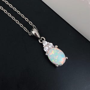 May include: A silver chain necklace with a white opal pendant. The pendant is surrounded by small clear cubic zirconia stones.