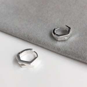 Puede incluir: Un par de pendientes de aro hexagonales de plata. Los pendientes son simples y modernos, y serían una gran adición a cualquier colección de joyas.