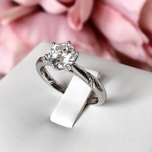 May include: A silver engagement ring with a large, round, clear diamond in the center. The band is twisted and has smaller diamonds set into it.