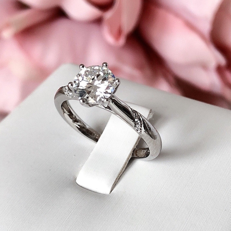 May include: A silver engagement ring with a large, round, clear diamond in the center. The band is twisted and has smaller diamonds set into it.