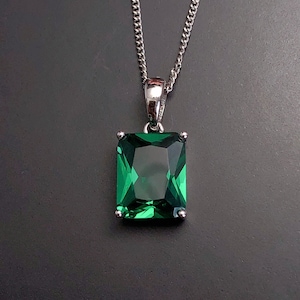 Puede incluir: Un collar de cadena de plata con un colgante que presenta una gran piedra preciosa verde esmeralda cortada en forma rectangular.