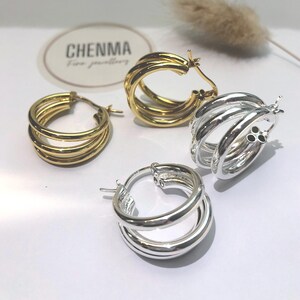 May include: Two pairs of hoop earrings, one pair is gold and the other is silver. Both pairs have three hoops.