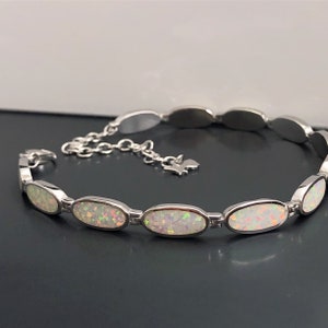 May include: A silver bracelet featuring oval-shaped white opals. The bracelet has a delicate chain extender.