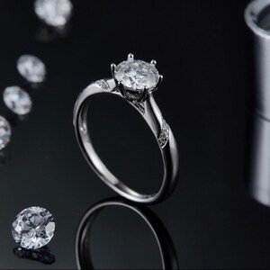 May include: A silver engagement ring with a large, clear, round-cut diamond center stone and smaller diamonds set in the band.