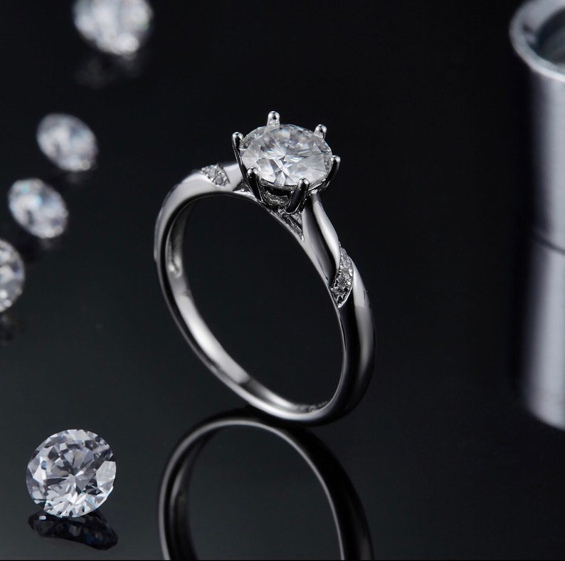 May include: A silver engagement ring with a large, clear, round-cut diamond center stone and smaller diamonds set in the band.