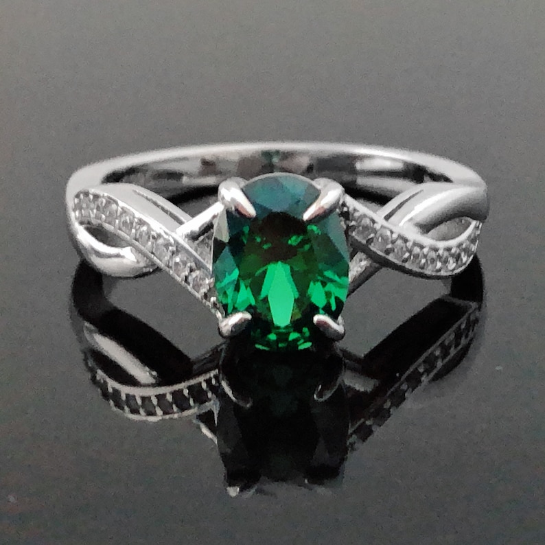 Puede incluir: Un anillo de plata con una piedra preciosa verde y peque&ntilde;as piedras transparentes engastadas en una banda retorcida.