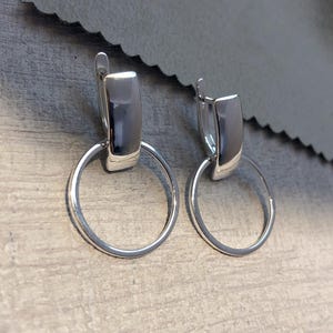 May include: Silver hoop earrings with a rectangular bar hanging from the top of each hoop.