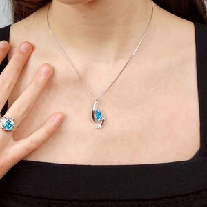 May include: A silver necklace with a pendant featuring a teardrop-shaped, light blue gemstone and a small, round, clear gemstone. A matching ring with a similar design is also visible.