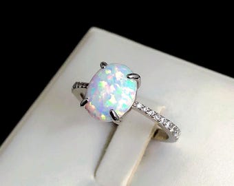 May include: A silver ring with a white opal gemstone and a band of small clear stones.