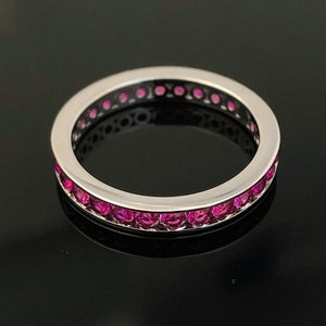 May include: A silver band ring with a row of pink gemstones around the entire band.